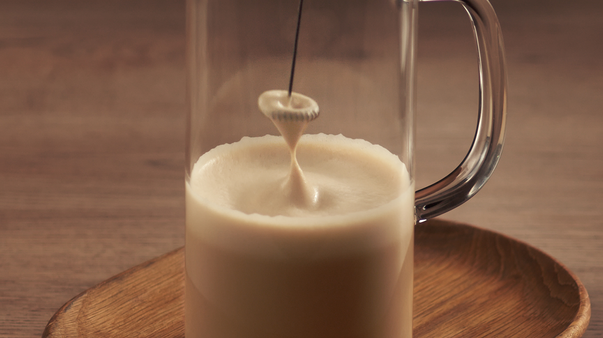 кофе с молоком в прозрачном графине взбивается капучинатором