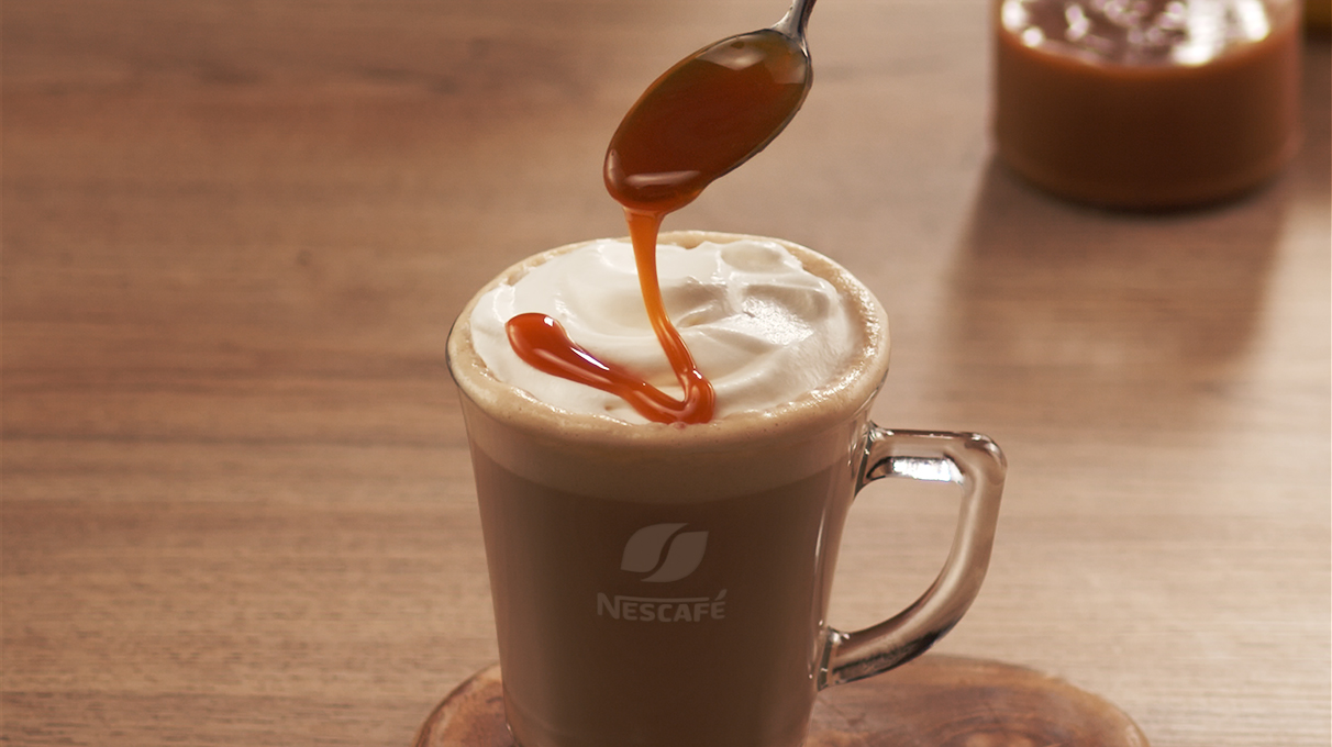 кофе латте в прозрачном бокале украшается карамельным сиропом